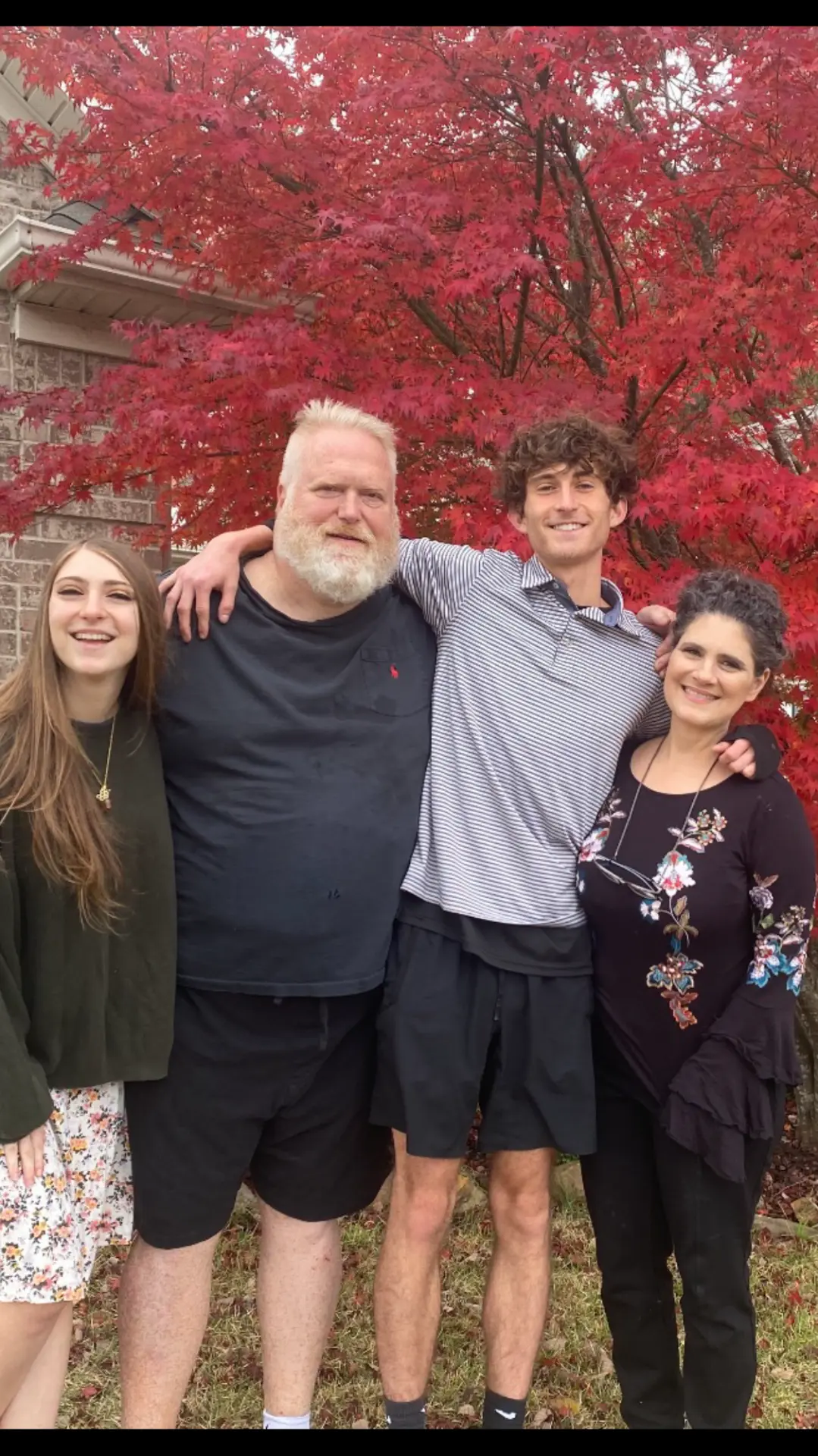 The Crowder family together outdoors in front of a red maple tree